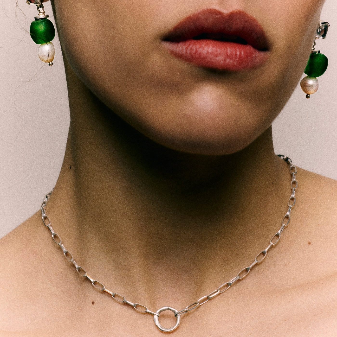 Close-up of a person wearing green earrings and a silver necklace.