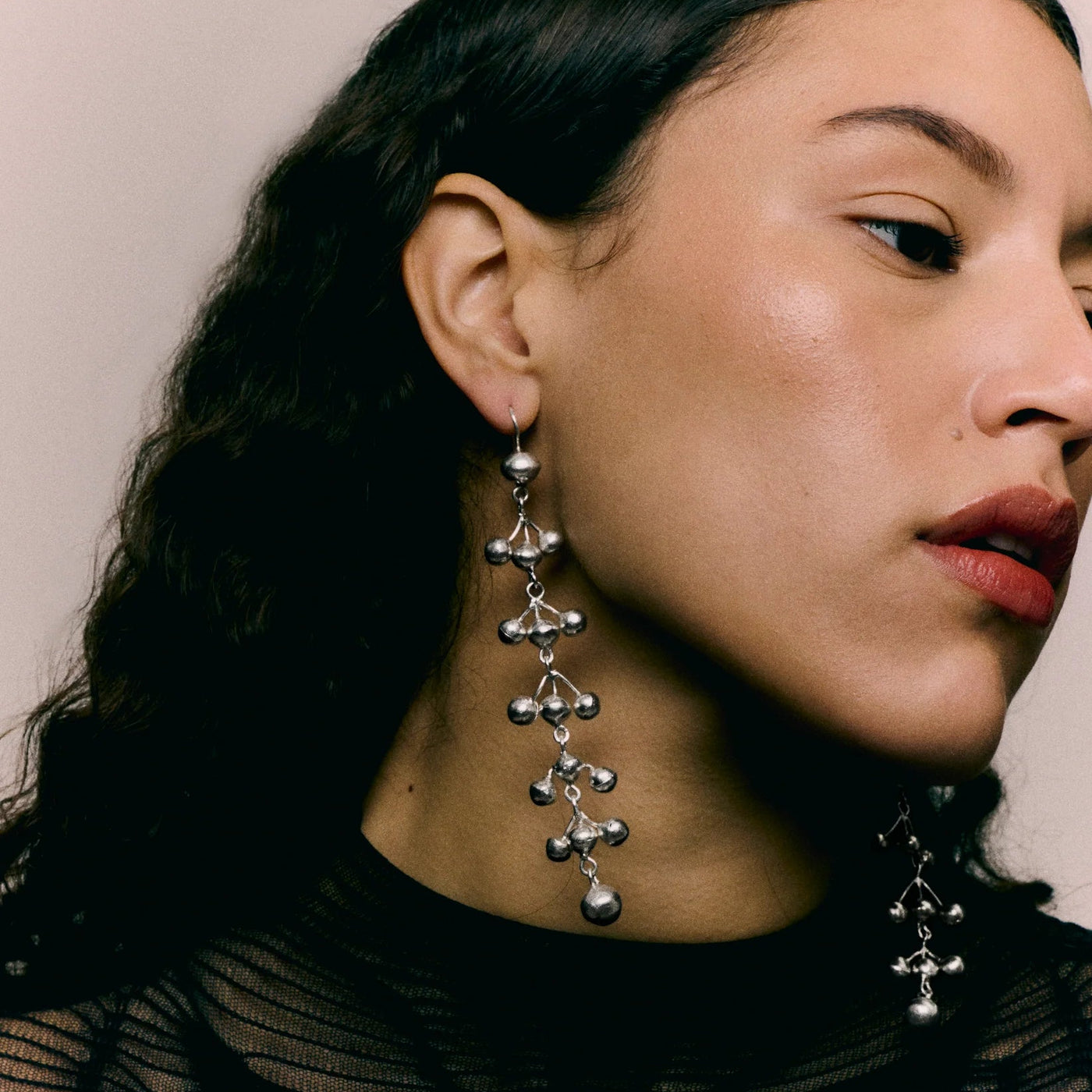 Close-up of a woman wearing silver dangling earrings with a neutral background