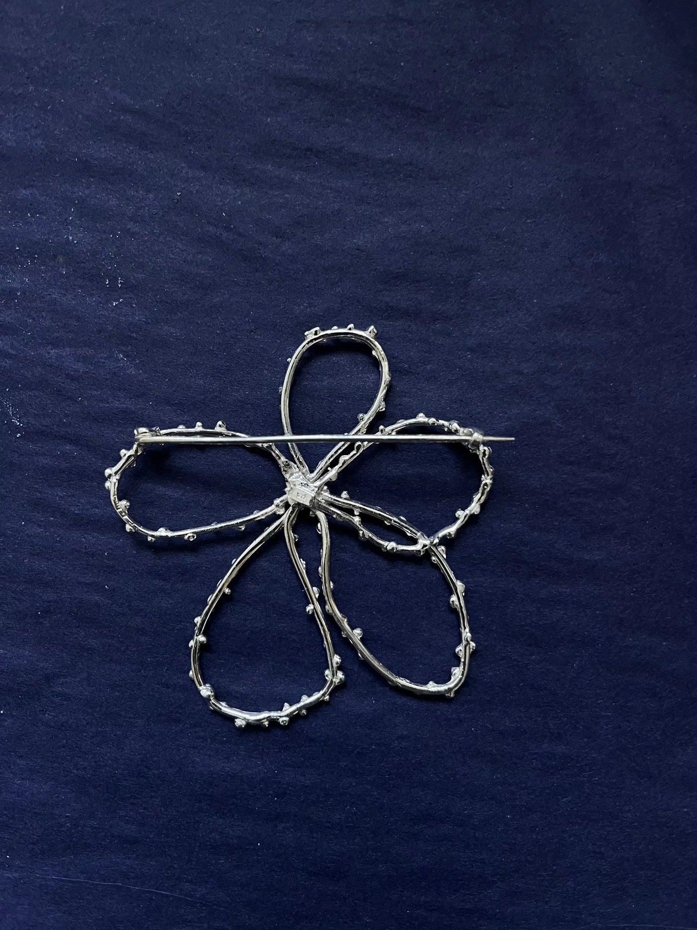 Silver brooch shaped like a four-leaf clover on a dark blue fabric background