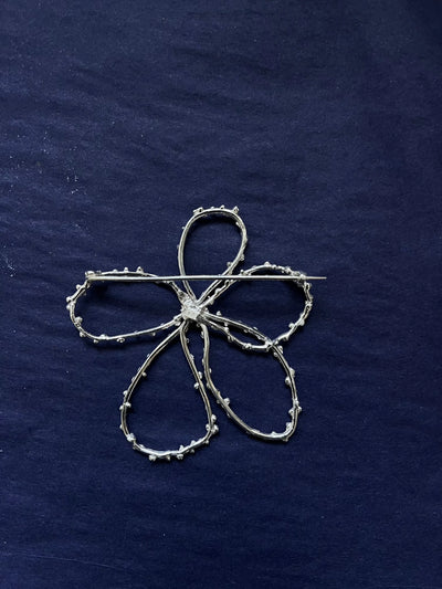 Silver brooch shaped like a four-leaf clover on a dark blue fabric background