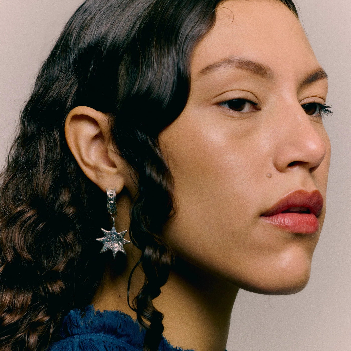 Close-up of a person wearing a blue top and star-shaped earrings against a neutral background