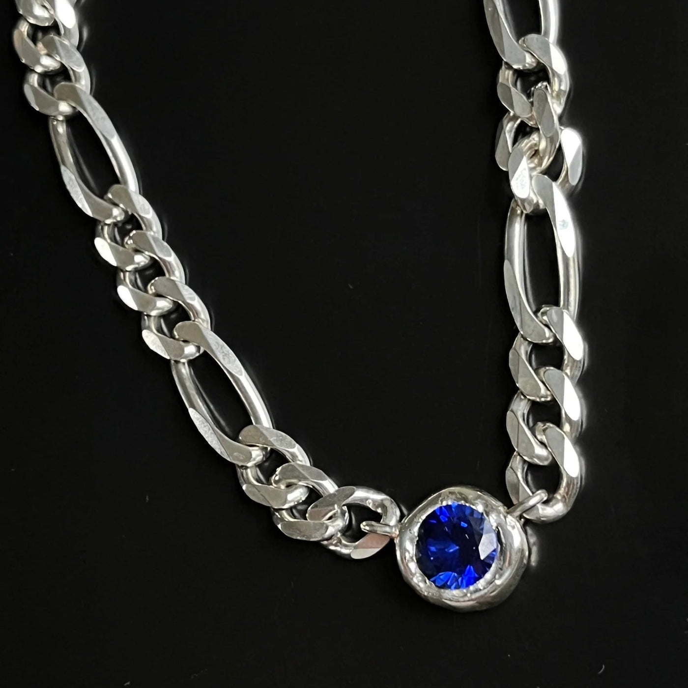 Silver chain bracelet with a blue gemstone on a black background