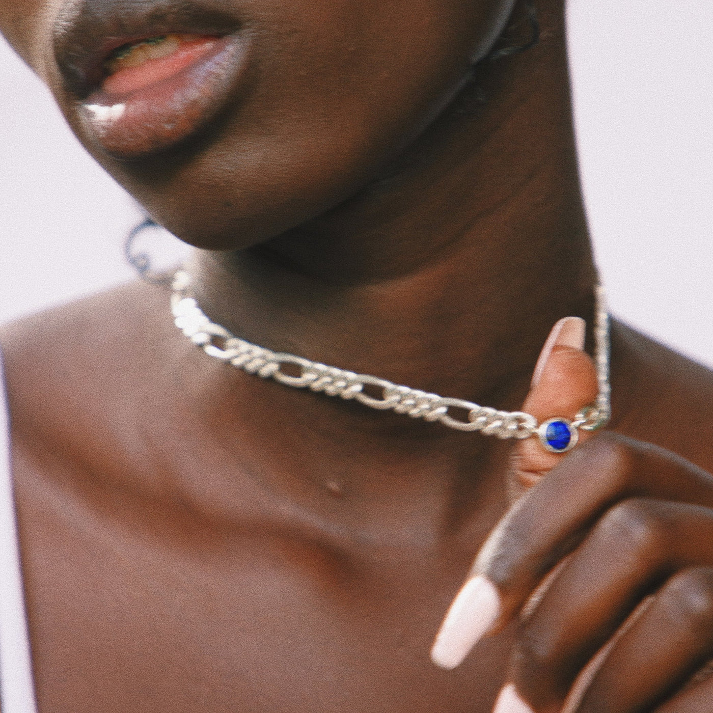 Close-up of a person wearing a silver chain necklace with a blue pendant.