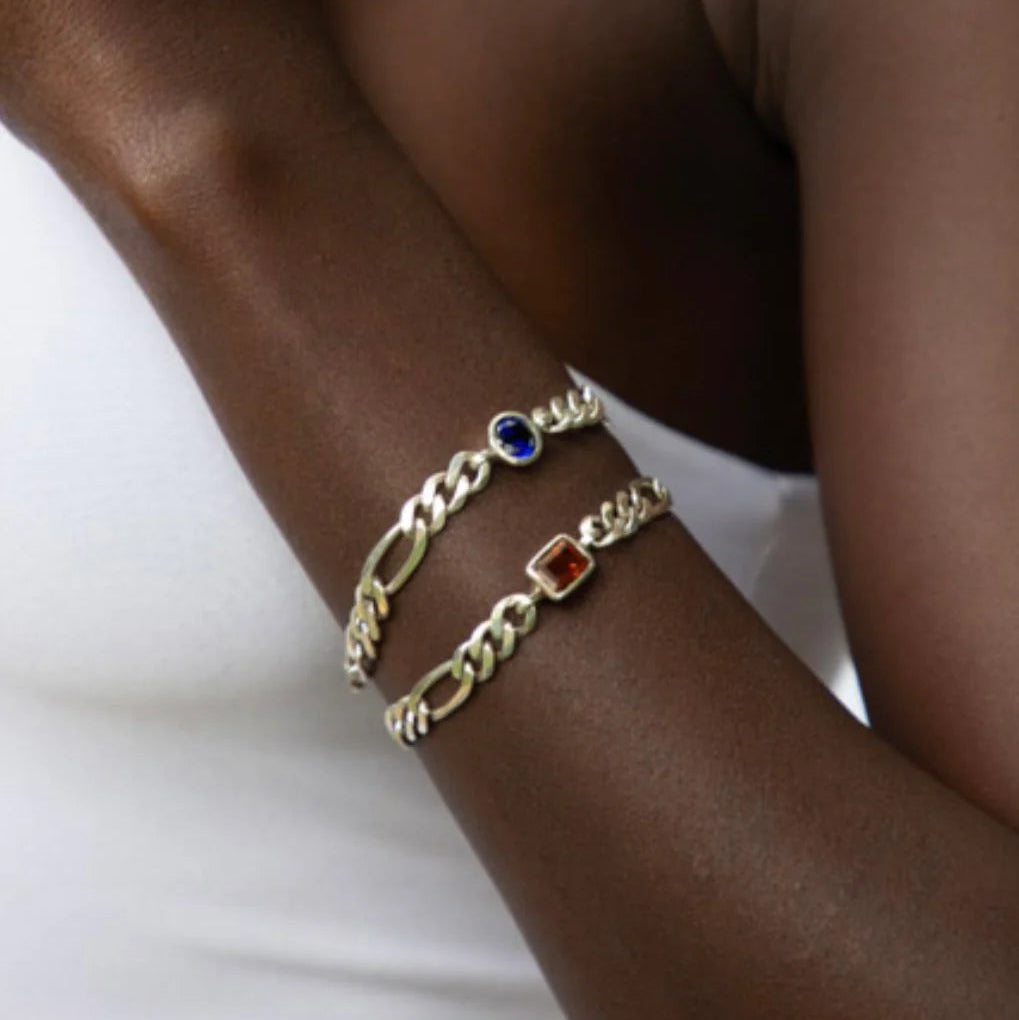 Gold chain bracelets with colored stones on a wrist against a white background