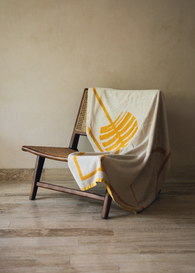 Beige towel with yellow design draped over a wooden chair against a beige wall.