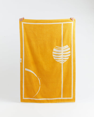 Yellow towel with white abstract design held by two hands on a light gray background