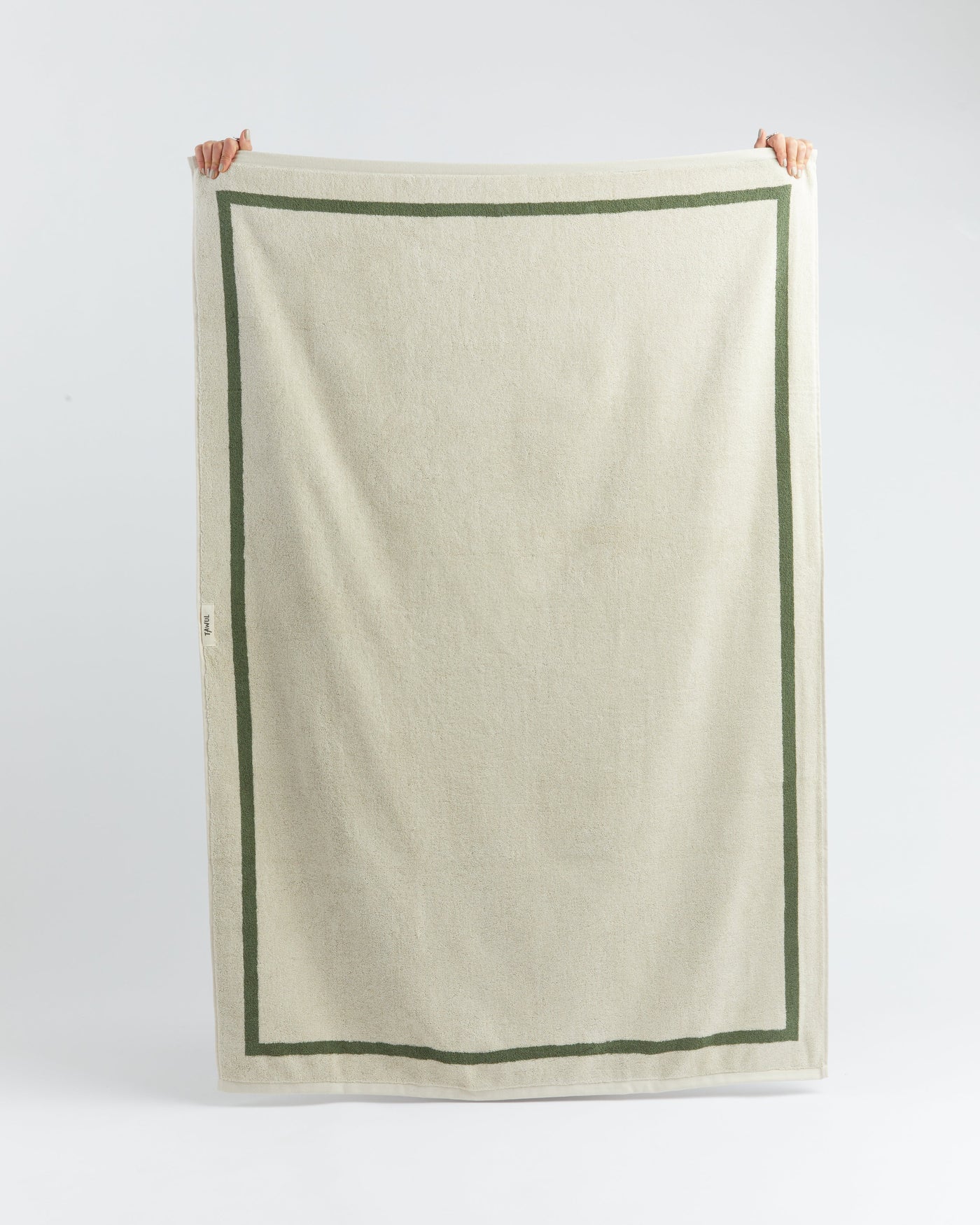 Beige towel with green border held up against a white background