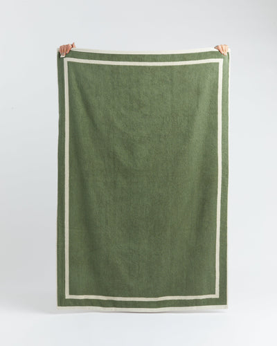 Green towel with white border held up against a light gray background
