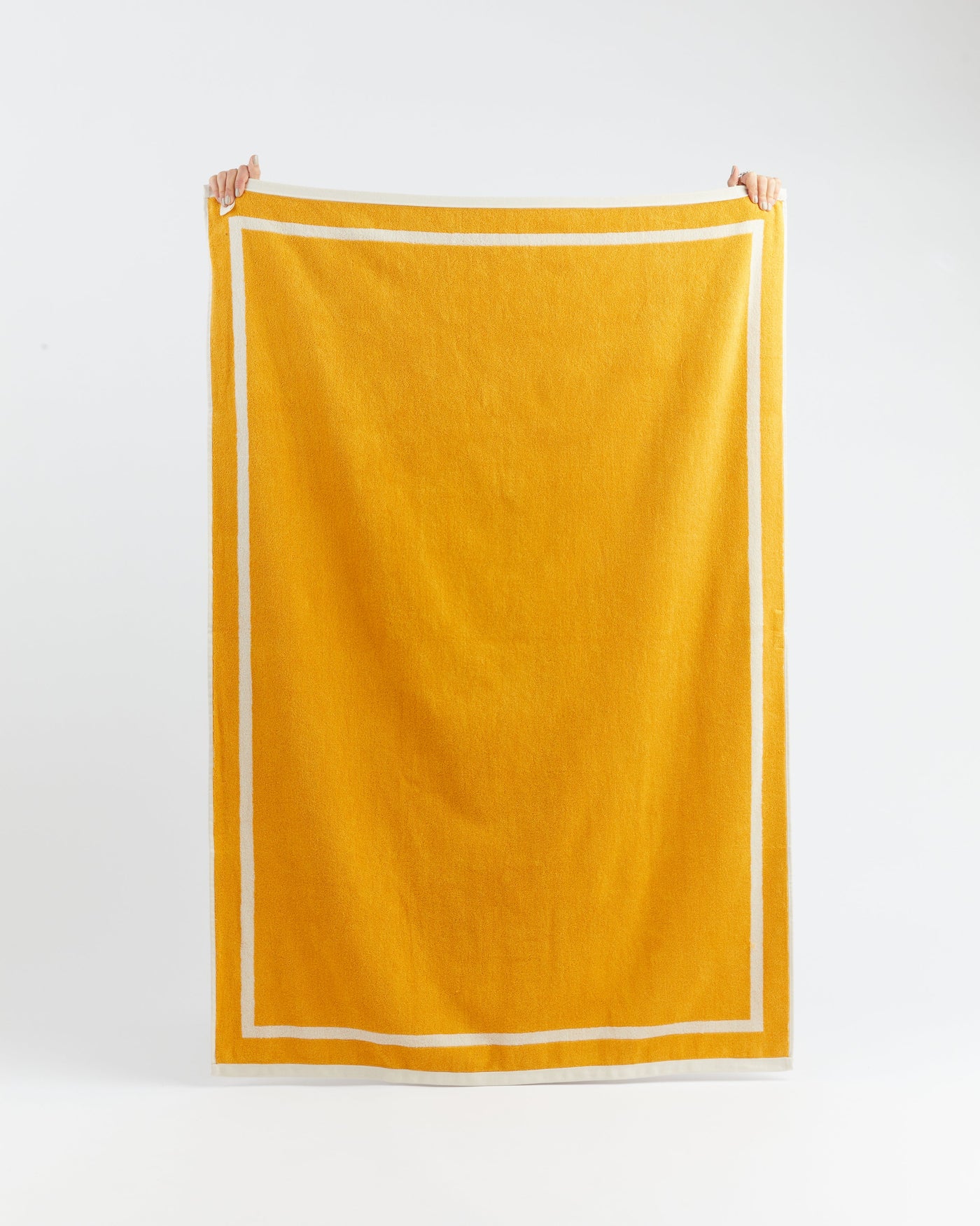 Yellow towel with white border held by two hands on a white background