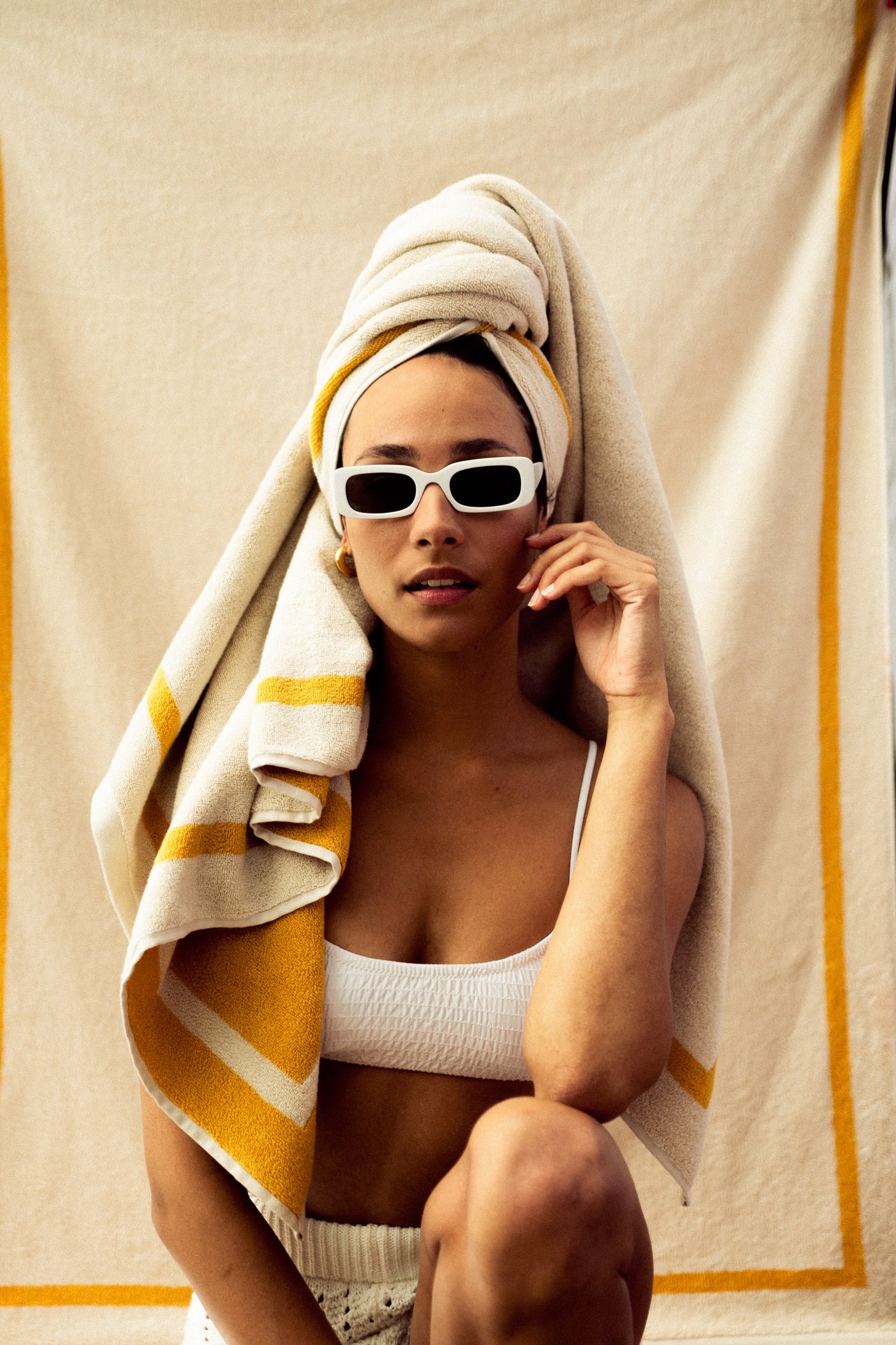 Woman wrapped in a towel with sunglasses, sitting on a textured surface