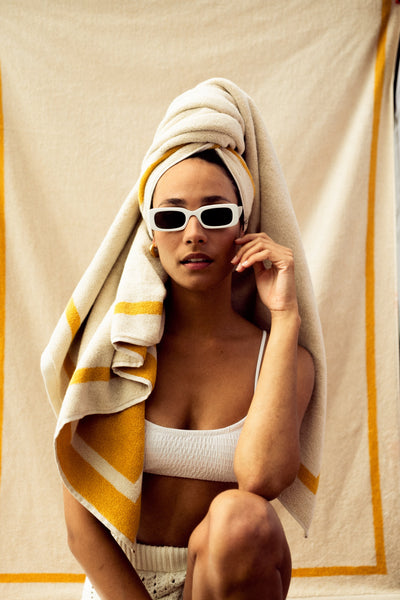 Woman wrapped in a towel with sunglasses, sitting on a textured surface