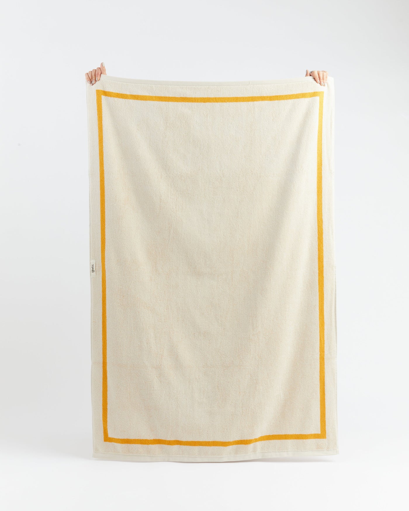 Beige towel with a yellow border held by two hands on a white background