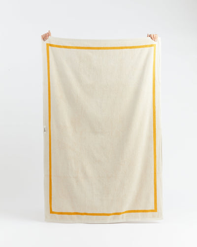 Beige towel with a yellow border held by two hands on a white background