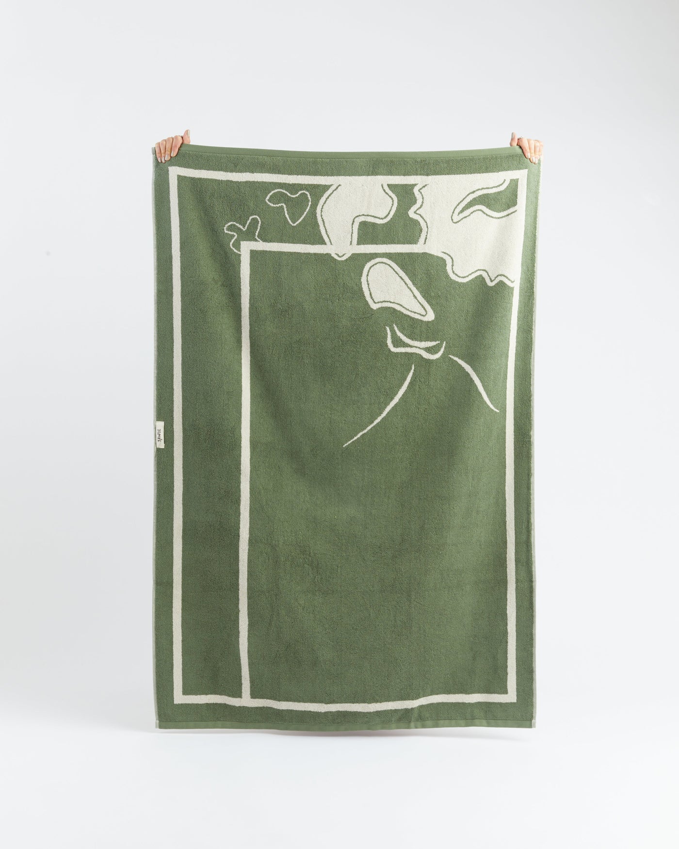 Green towel with white abstract design held by two hands on a white background