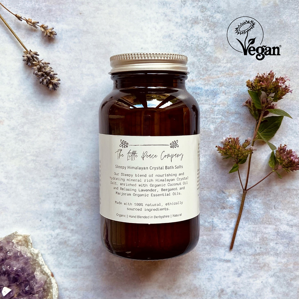 A jar of The Little Peace Company Sleepy Himalayan Crystal Bath Salts with ingredients like lavender and Bergamot leaves scattered around, emphasizing its natural and organic qualities.