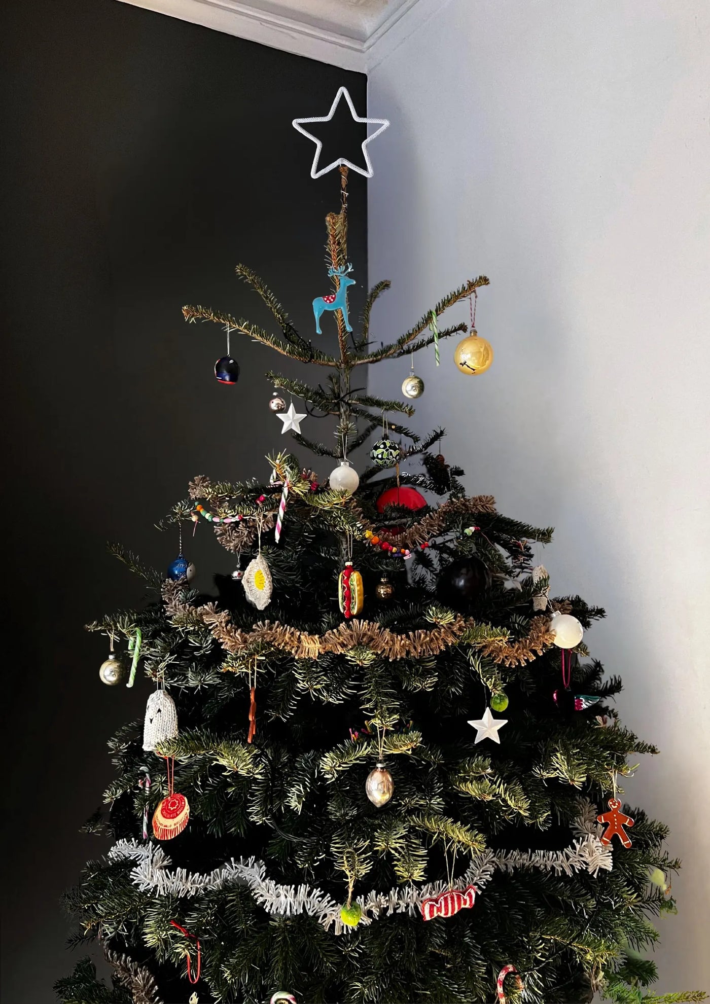 Decorated Christmas tree with various ornaments against a dark wall.