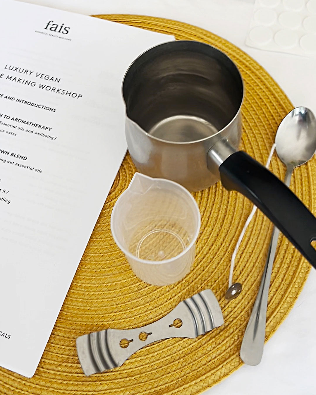 Metal measuring cup, spoon, and small container on a yellow woven mat with a magazine underneath.