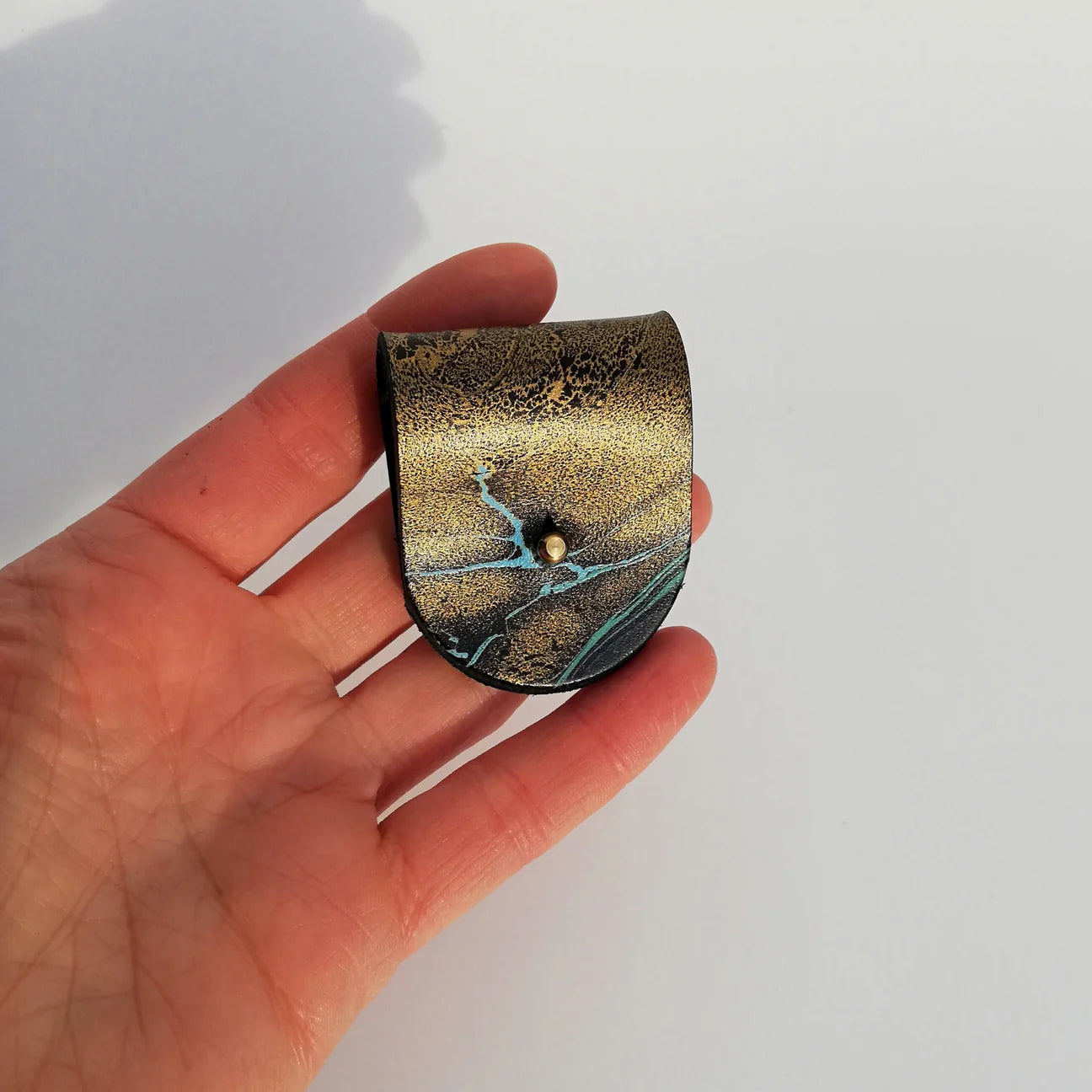 Hand holding a small, decorative item with gold and green marbled design on a white background