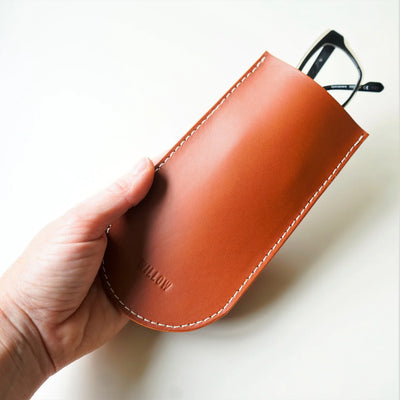 Brown leather glasses case held by a hand on a white background