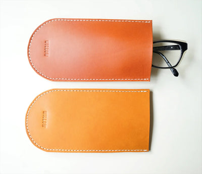 Two brown leather eyeglass cases with a pair of black-framed glasses on a white background.