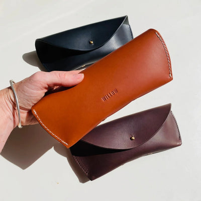 Brown leather clutch held by a hand with two other clutches on a light background
