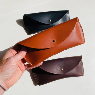 Three leather pouches in black, brown, and dark brown held by a hand on a light background.