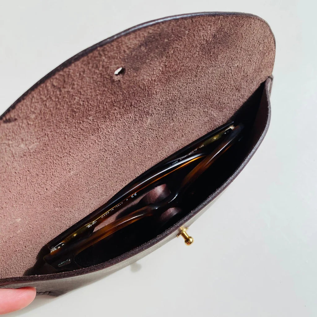 Brown suede clutch with sunglasses inside on a light gray background